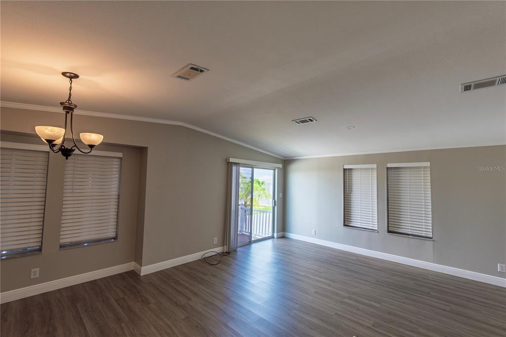 An empty living room features gray walls, wood-look flooring, a chandelier, and sliding glass doors — 25 COPENHAGEN AVENUE, PUNTA GORDA, FL