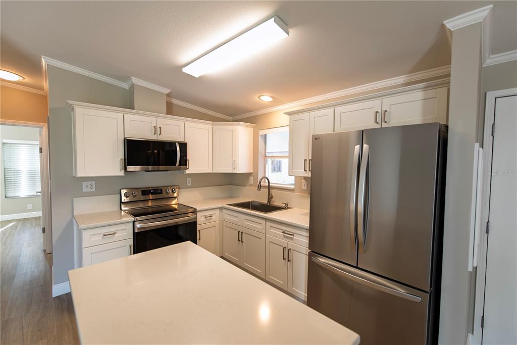 A kitchen features white cabinets, stainless steel appliances, a kitchen island, and quartz countertops — 25 COPENHAGEN AVENUE, PUNTA GORDA, FL