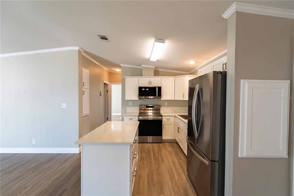A kitchen features white cabinets, stainless steel appliances, a center island, and wood-look flooring — 25 COPENHAGEN AVENUE, PUNTA GORDA, FL