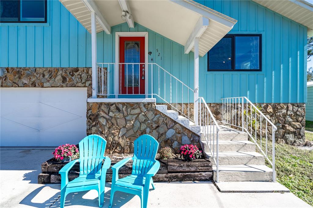 A blue house with a stone base, red front door, and two turquoise chairs outside — 521 PAMETO ROAD, NOKOMIS, FL
