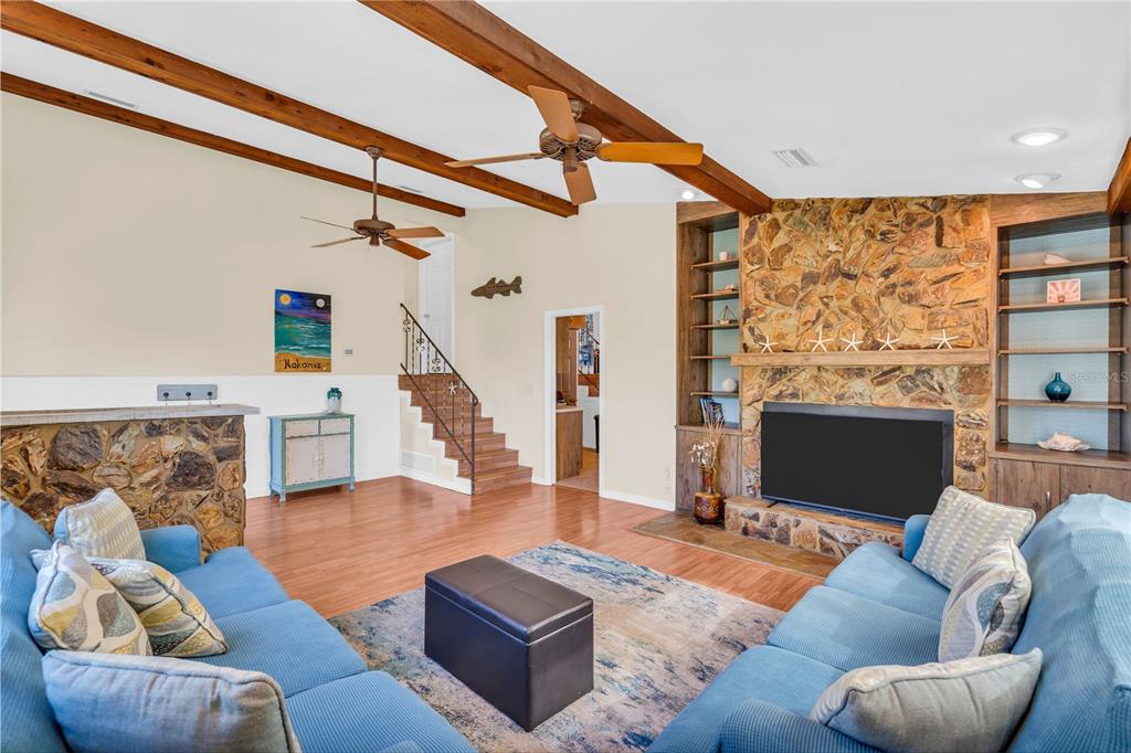 A living room features a stone fireplace, wood-beamed ceilings, blue sofas, and a staircase — 521 PAMETO ROAD, NOKOMIS, FL