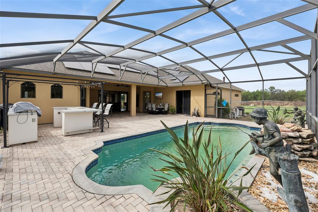 A screened-in patio features a swimming pool, a stone statue, and an outdoor kitchen area — 7139 GROVELAND FARMS ROAD, GROVELAND, FL