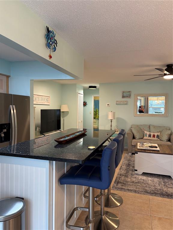 A kitchen island with dark countertops and blue bar stools faces a living area — 14531 WALSINGHAM ROAD UNIT 224, LARGO, FL