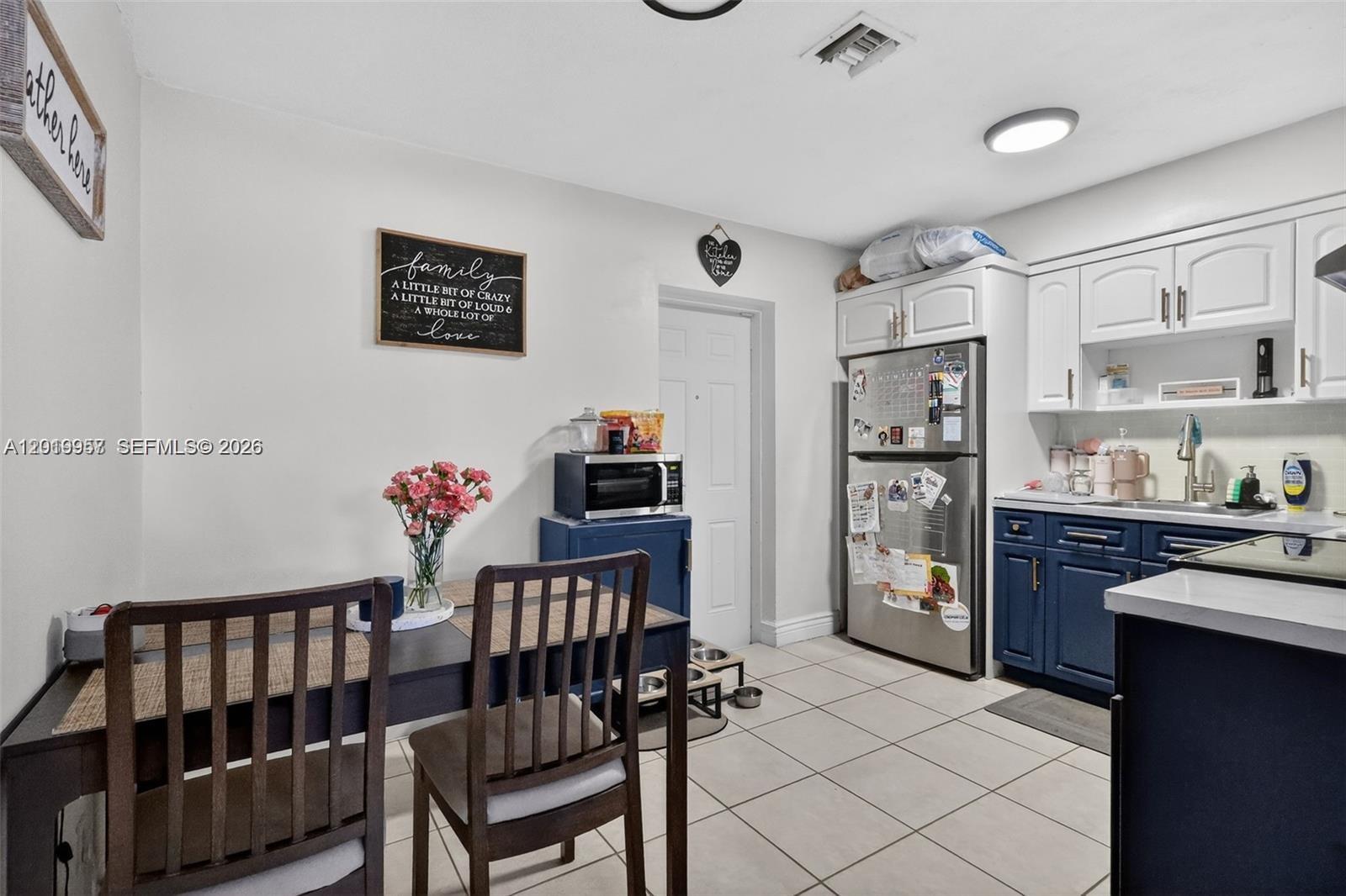 A kitchen features blue lower cabinets, white upper cabinets, a stainless steel refrigerator, and dining area — 6791 Scott St, Hollywood FL 33024, HOLLYWOOD, FL