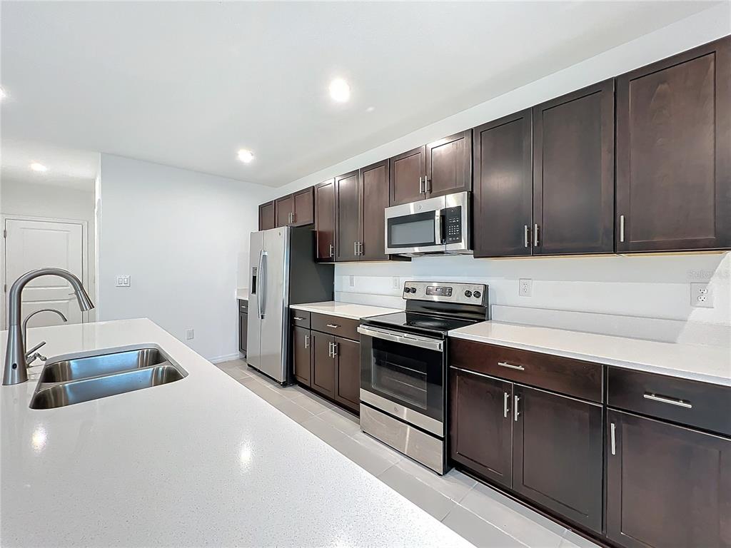 A modern kitchen features dark wood cabinets, stainless steel appliances, and white quartz countertops — 5627 COSTA BLANCA WAY, DAVENPORT, FL