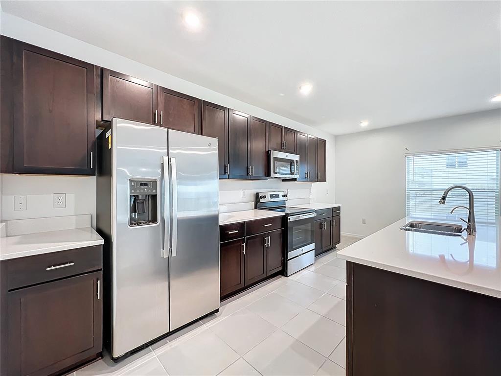 A kitchen features dark wood cabinets, stainless steel appliances, white countertops, and a center island — 5627 COSTA BLANCA WAY, DAVENPORT, FL