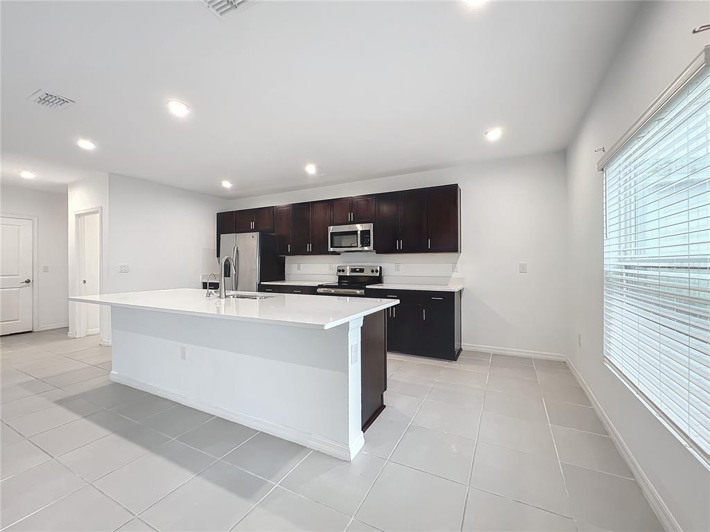 A kitchen with dark wood cabinets, white countertops, a central island, and light tile flooring — 5627 COSTA BLANCA WAY, DAVENPORT, FL