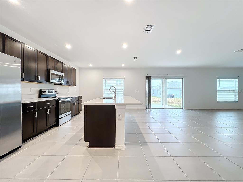 A kitchen with dark cabinets, stainless steel appliances, and a central island with white countertops — 5627 COSTA BLANCA WAY, DAVENPORT, FL