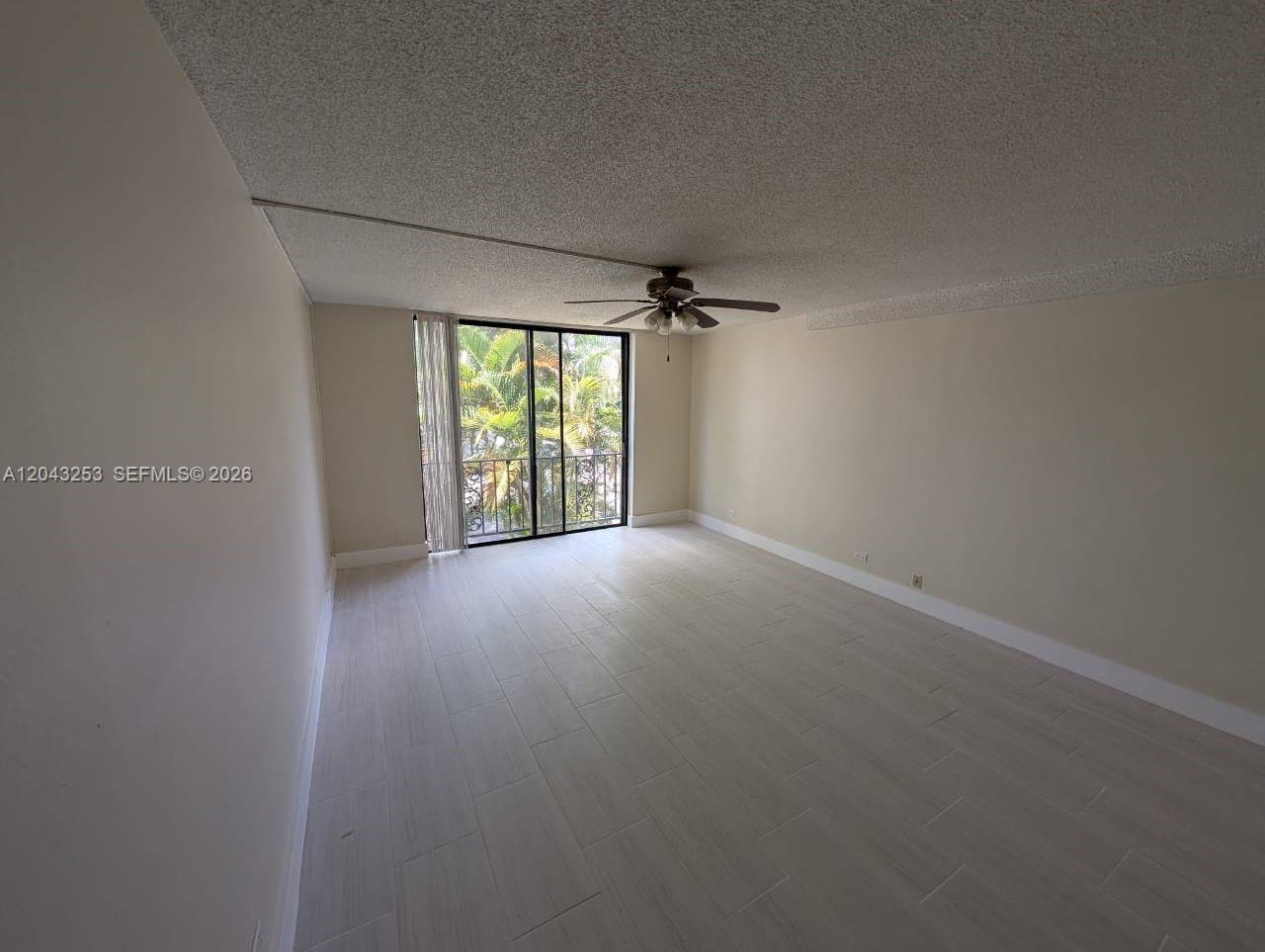An empty room features light-colored tile flooring, a ceiling fan, and a sliding glass door — 3680 Inverrary Dr # 2M, Lauderhill FL 33319, LAUDERHILL, FL