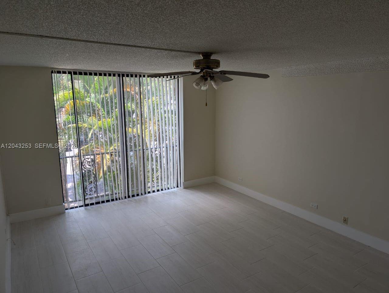An empty room features light-colored tile flooring, a ceiling fan, and floor-to-ceiling vertical blinds — 3680 Inverrary Dr # 2M, Lauderhill FL 33319, LAUDERHILL, FL
