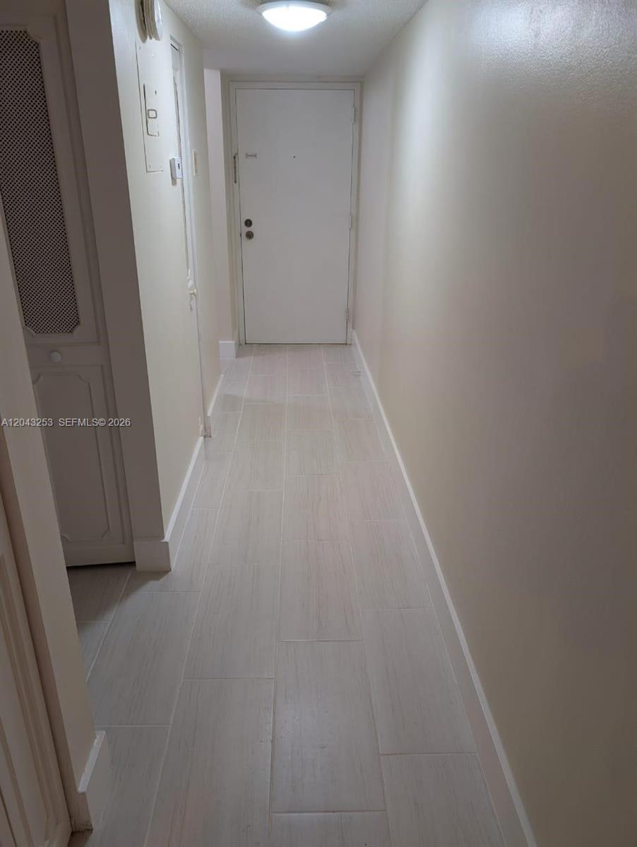 A narrow hallway features light-colored wood-look tile flooring, beige walls, and a white entry door — 3680 Inverrary Dr # 2M, Lauderhill FL 33319, LAUDERHILL, FL