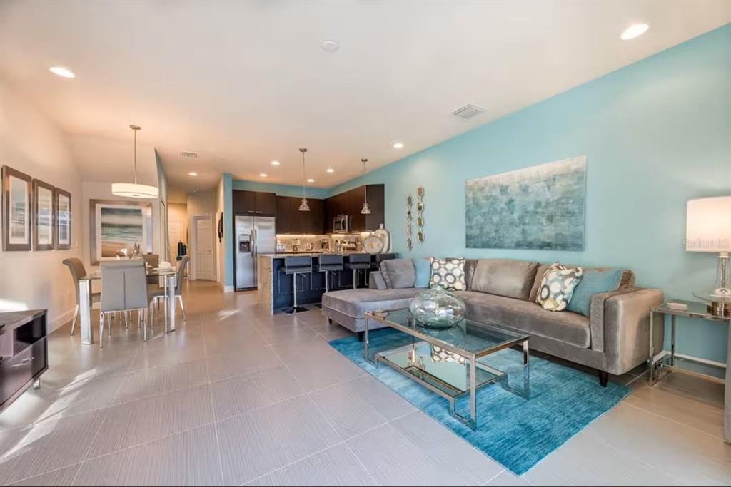 An open-concept living and dining area features a kitchen island, gray sofa, and blue rug — 1425 RETREAT CIRCLE, CLERMONT, FL
