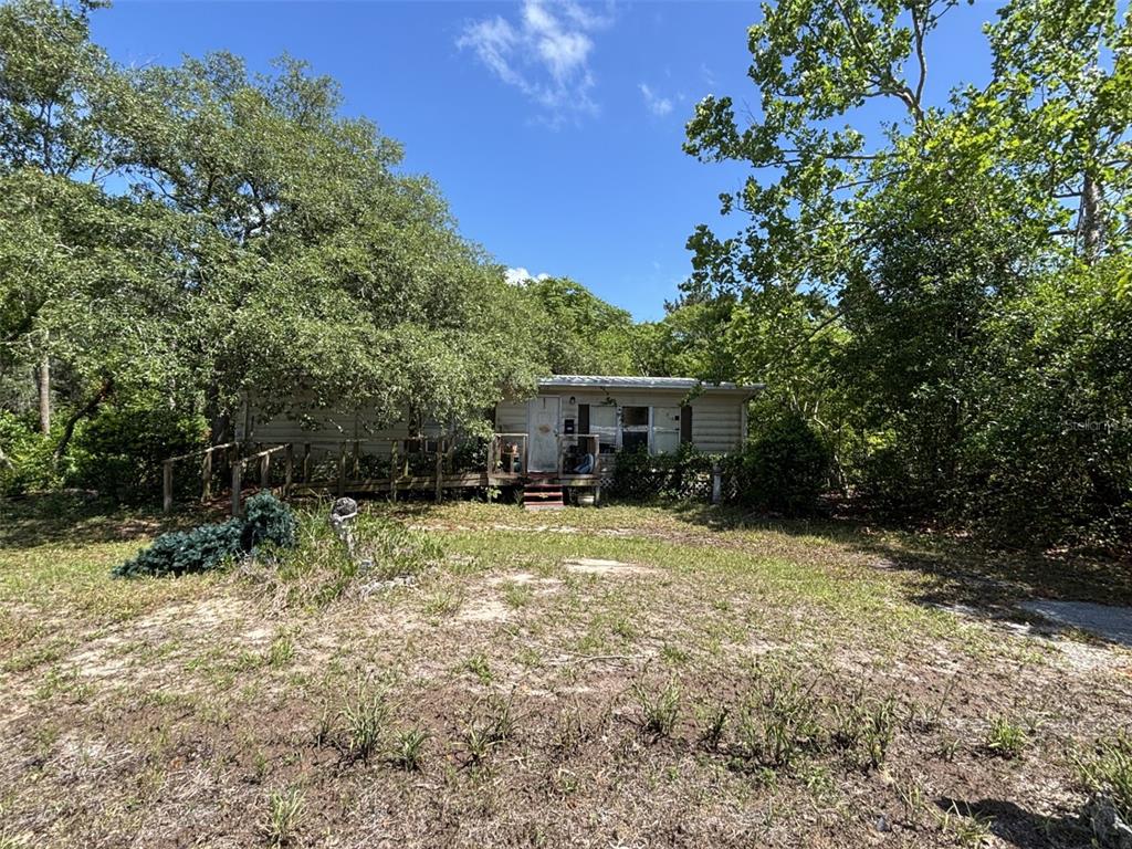 A single-story mobile home with a wooden porch sits on a grassy, wooded lot — 12506 WALTON AVENUE, NEW PORT RICHEY, FL
