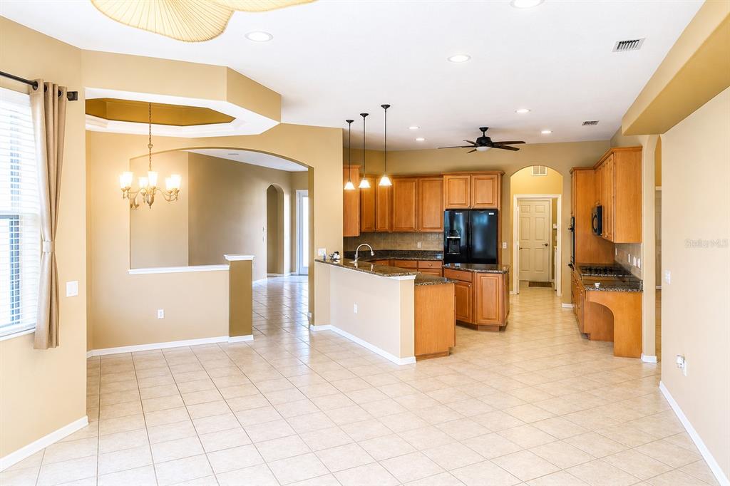 An open-concept kitchen with wood cabinets and granite countertops overlooks a tiled dining area — 14024 NIGHTHAWK TERRACE, LAKEWOOD RANCH, FL
