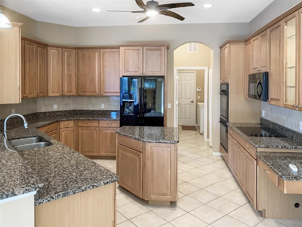 A kitchen features light wood cabinets, granite countertops, a black refrigerator, and tile flooring — 14024 NIGHTHAWK TERRACE, LAKEWOOD RANCH, FL