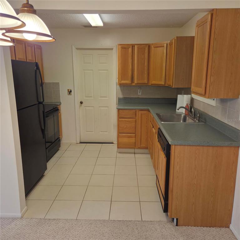 A kitchen features oak cabinets, green laminate countertops, black appliances, and white tile flooring — 3825 97TH AVENUE N UNIT n/a, PINELLAS PARK, FL