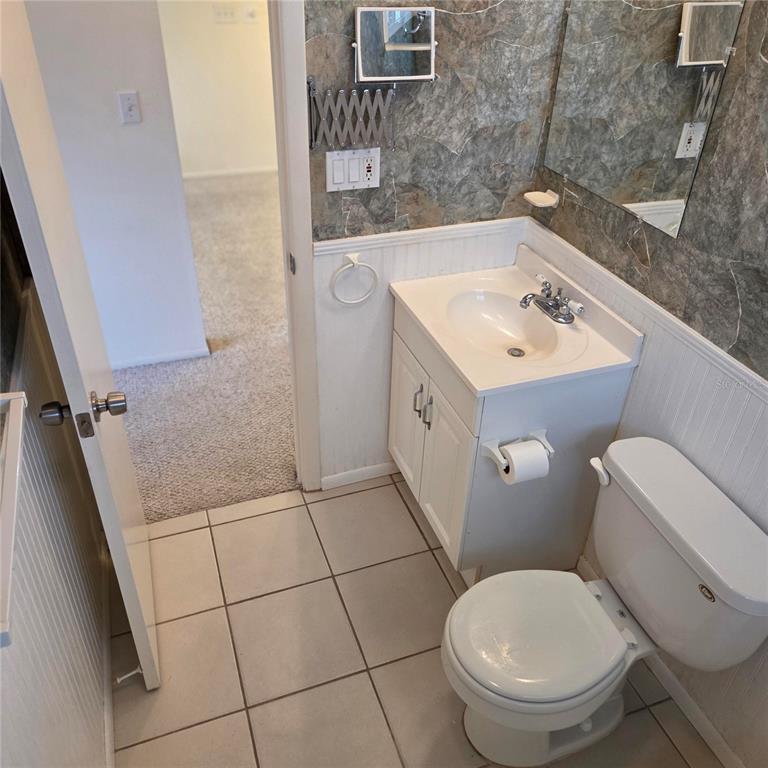 A small bathroom features a white vanity, a toilet, and stone-look wall tiles — 3825 97TH AVENUE N UNIT n/a, PINELLAS PARK, FL