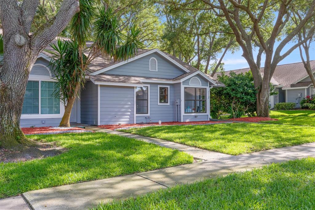 An exterior view of a light blue single-story home with a brick walkway and landscaping — 2668 BENTLEY DRIVE, PALM HARBOR, FL