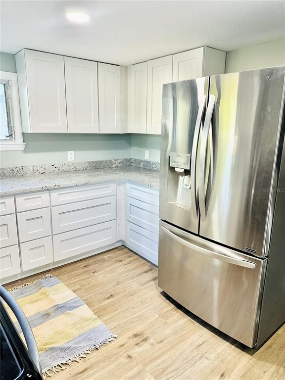 A kitchen features white cabinets, a stainless steel refrigerator, and light-colored wood-look flooring — 5654 12TH STREET, ZEPHYRHILLS, FL