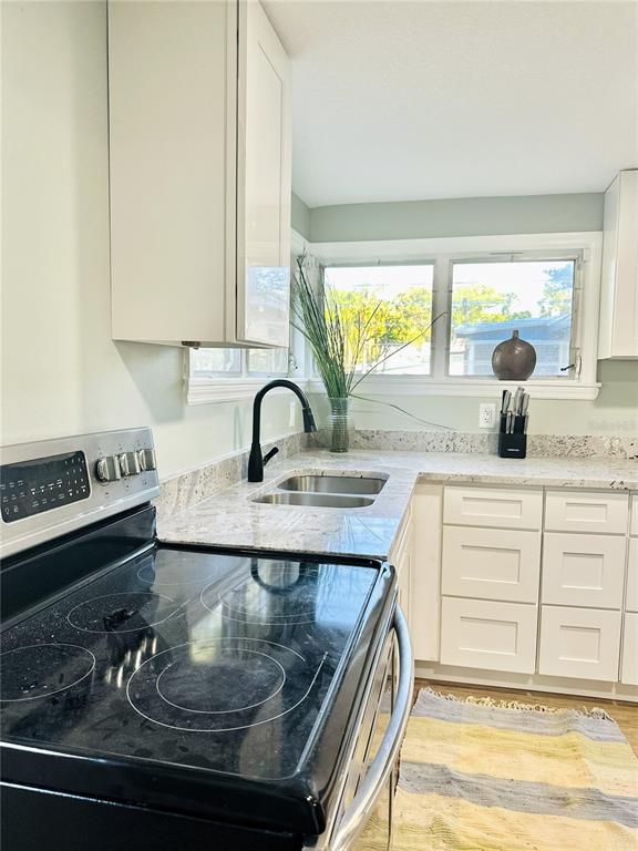 A kitchen features white cabinets, granite countertops, a black electric stove, and a double sink — 5654 12TH STREET, ZEPHYRHILLS, FL
