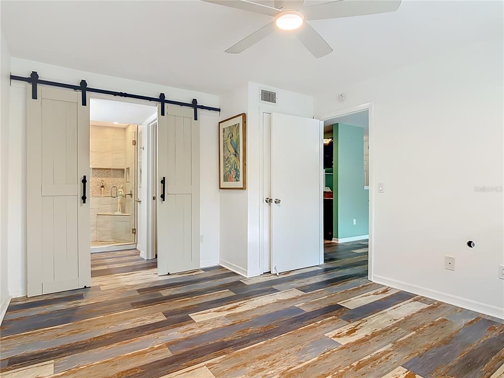 A bedroom features wood-look plank flooring, a ceiling fan, and sliding barn doors to a bathroom — 1401 S PALMETTO AVENUE UNIT 616, DAYTONA BEACH, FL