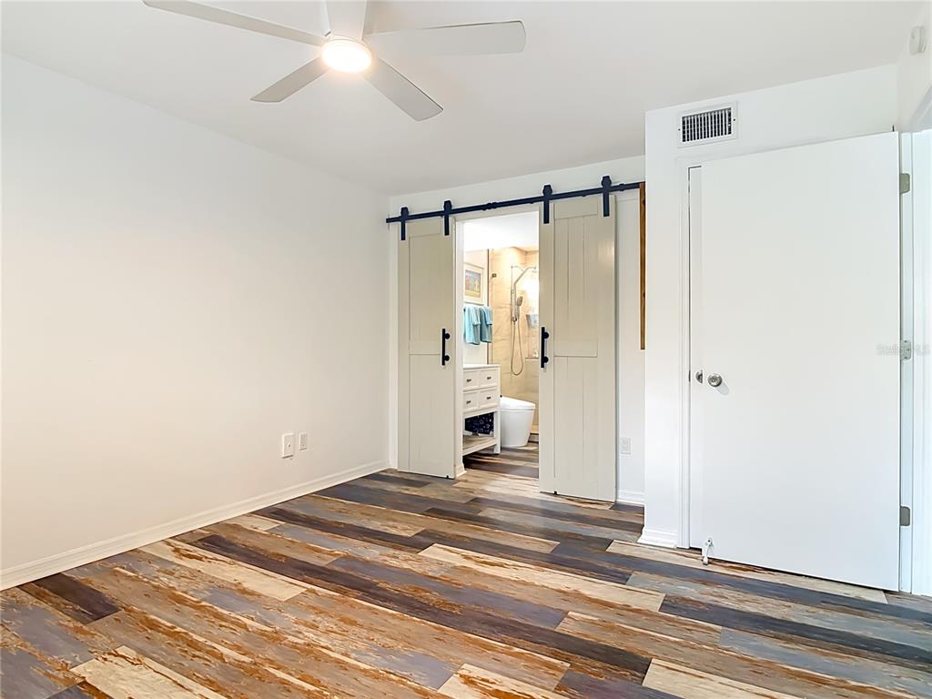 A bedroom with multi-toned wood-look flooring, a ceiling fan, and sliding barn doors to a bathroom — 1401 S PALMETTO AVENUE UNIT 616, DAYTONA BEACH, FL