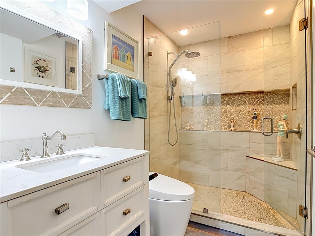 A bathroom features a white vanity, a glass-enclosed shower with pebble tile, and a toilet — 1401 S PALMETTO AVENUE UNIT 616, DAYTONA BEACH, FL