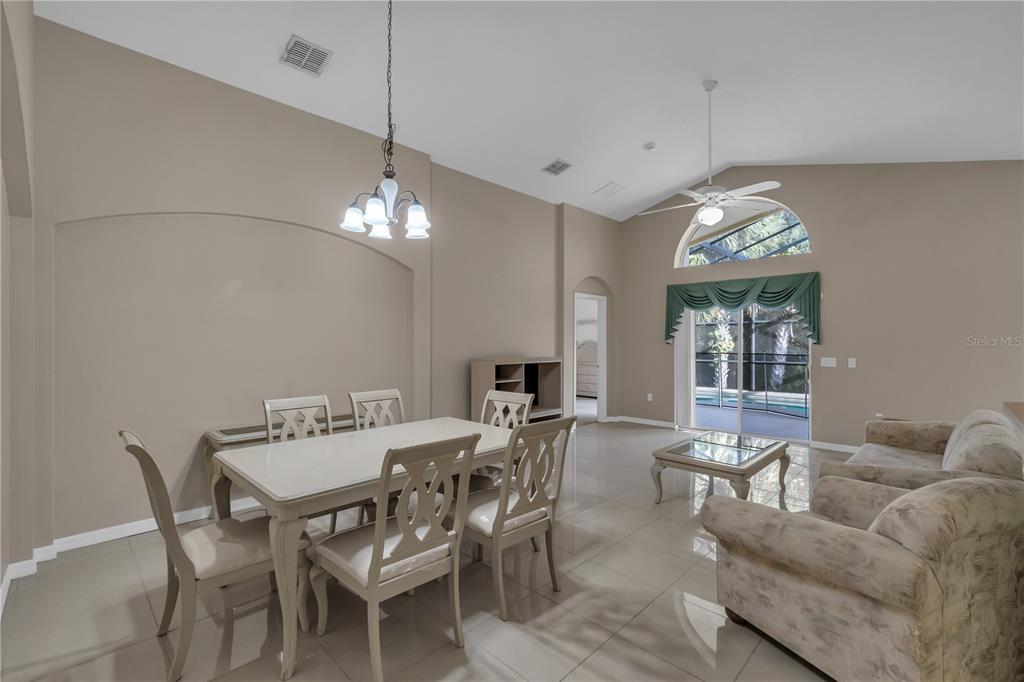 A dining and living area with vaulted ceilings, tile floors, and a sliding glass door — 4700 CUMBRIAN LAKES DRIVE, KISSIMMEE, FL