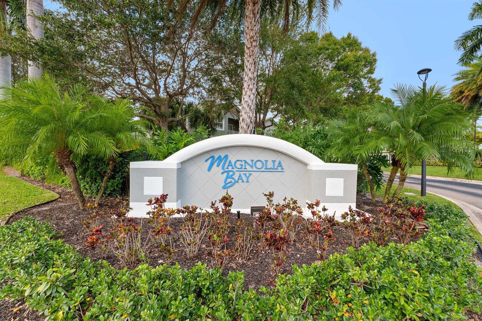 A community entrance sign for Magnolia Bay stands surrounded by palm trees and landscaping — 3105 Grandiflora Drive, FL 33467, FL