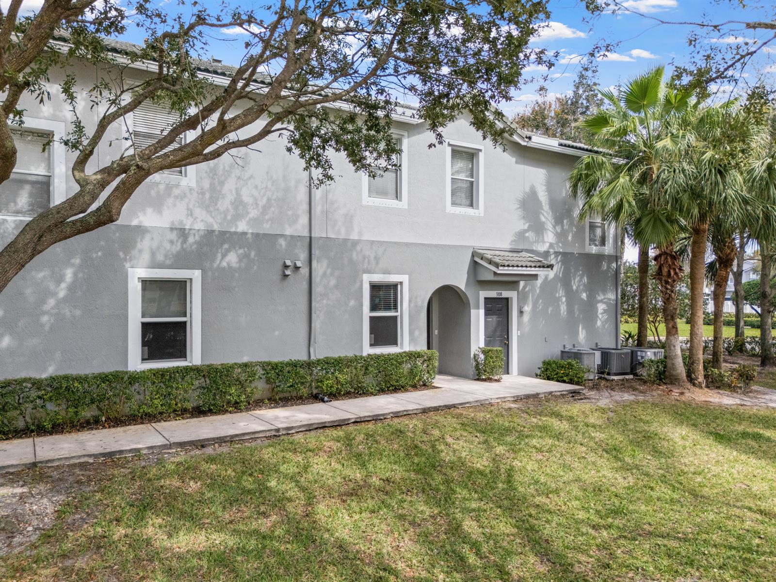 A two-story gray apartment building features a front entrance, a sidewalk, and palm trees — 3105 Grandiflora Drive, FL 33467, FL