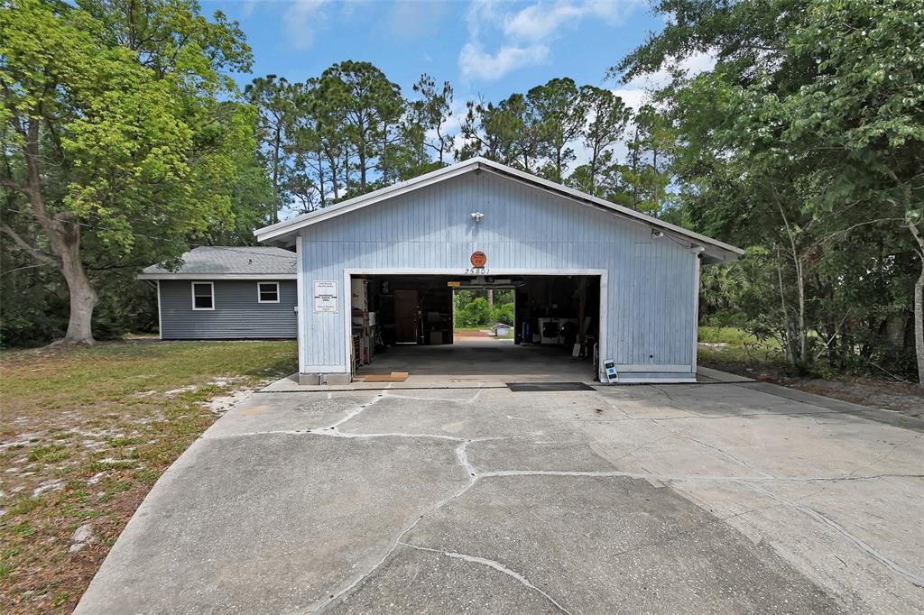 A detached light blue garage with a concrete driveway sits in front of a house — 25801 BLUE LAKES DRIVE, PAISLEY, FL