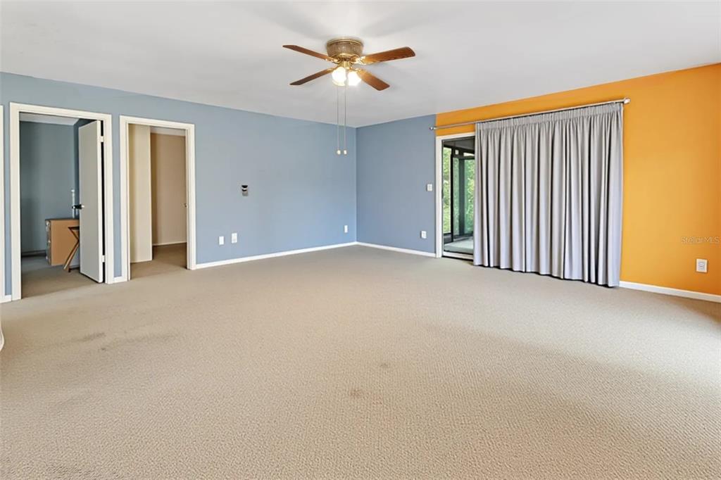 A spacious room features blue and orange walls, beige carpeting, and a ceiling fan — 25801 BLUE LAKES DRIVE, PAISLEY, FL