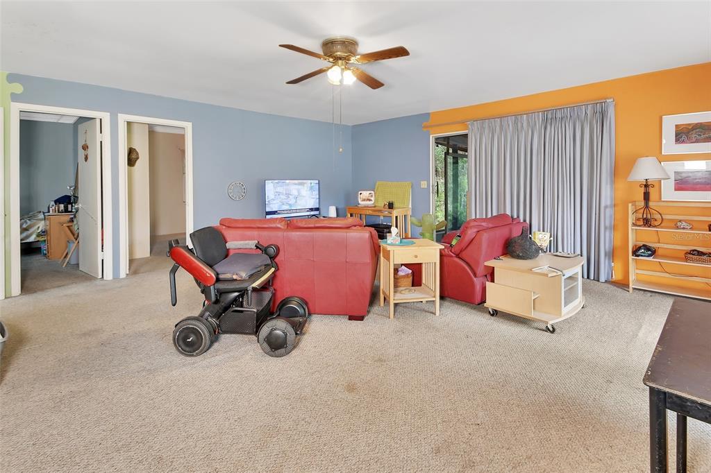 A living room features a red sofa, a power wheelchair, and blue and orange walls — 25801 BLUE LAKES DRIVE, PAISLEY, FL