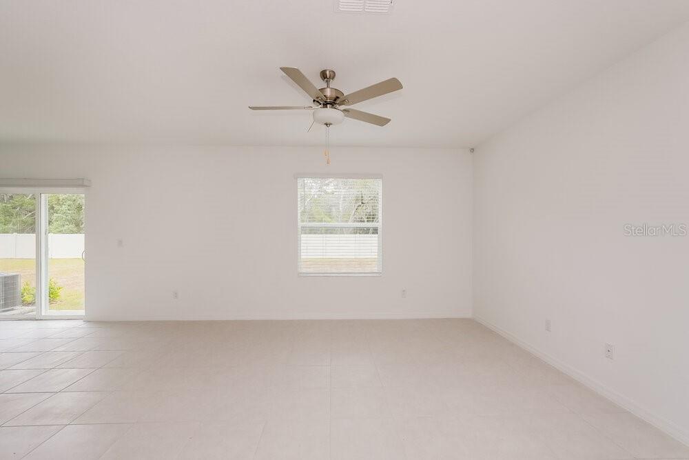 A bright, empty room features white walls, light tile flooring, a ceiling fan, and sliding doors — 17932 BLISSFUL STARS DRIVE, LUTZ, FL