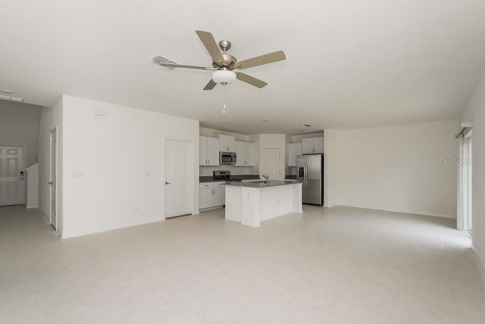 An open-concept kitchen and living area featuring white cabinets, a center island, and tile flooring — 17932 BLISSFUL STARS DRIVE, LUTZ, FL