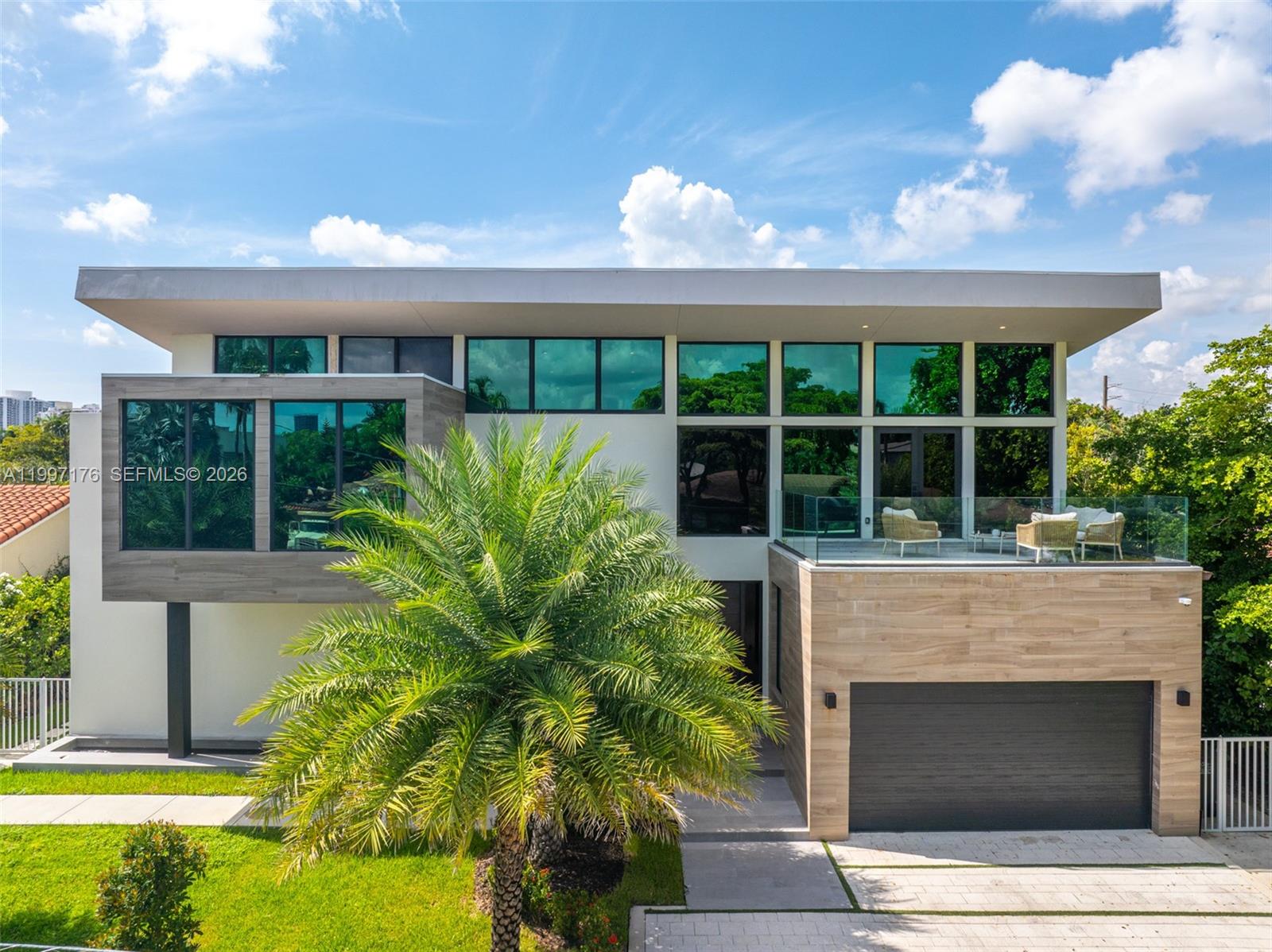 A modern two-story house features a wood-paneled garage, large glass windows, and a balcony — 521 Holiday Dr, Hallandale Beach FL 33009, HALLANDALE BEACH, FL