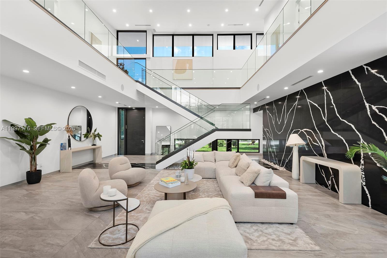 A modern, two-story living room features a glass staircase, white sofa, and black marble wall — 521 Holiday Dr, Hallandale Beach FL 33009, HALLANDALE BEACH, FL