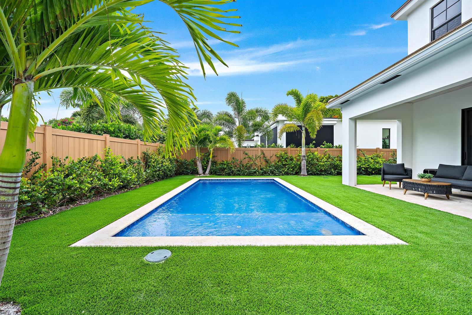 A backyard features a rectangular swimming pool, artificial turf, palm trees, and a covered patio — 309 Cascade Lane, Palm Beach Shores FL 33404, PALM BEACH SHORES, FL