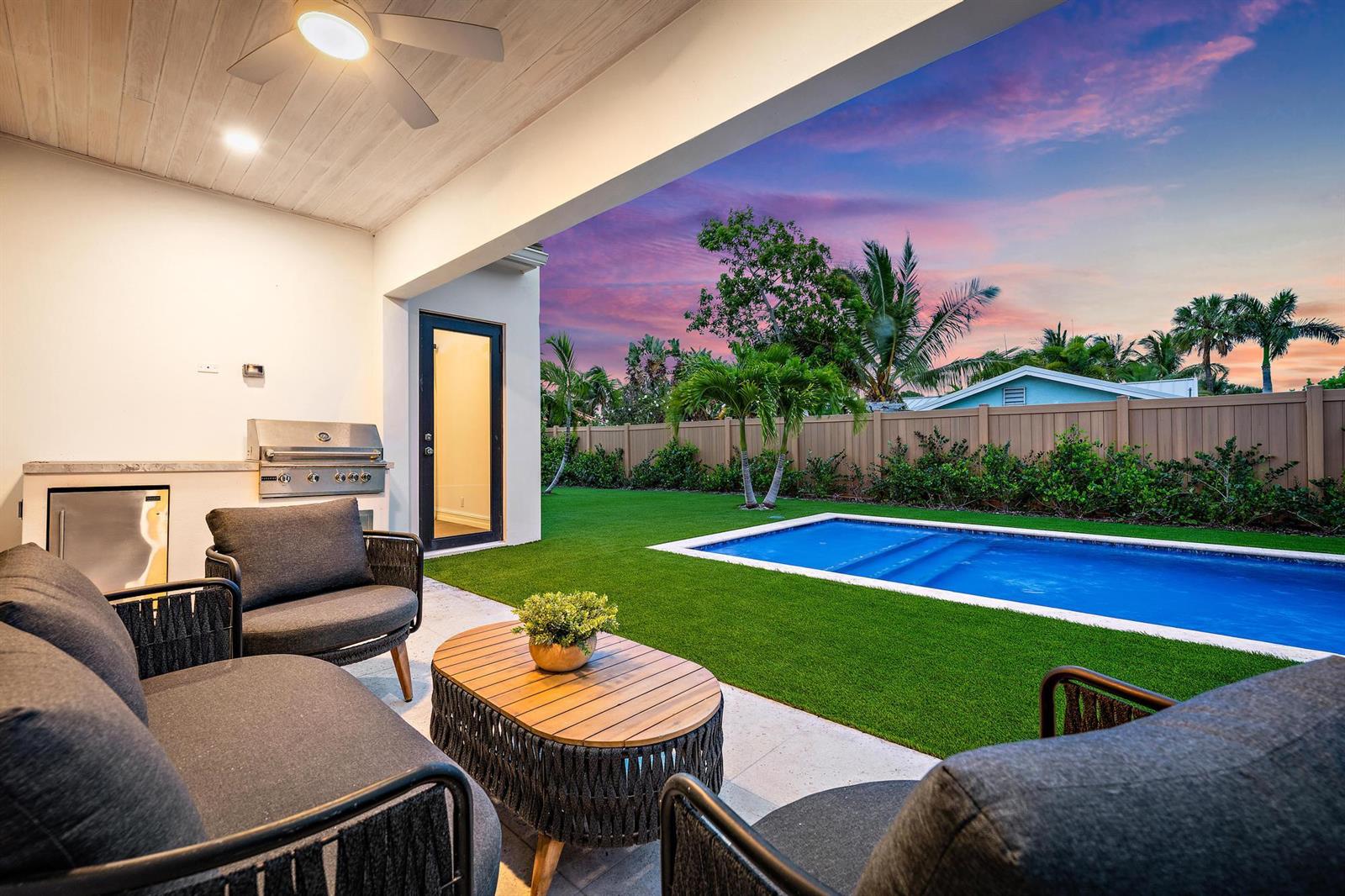 A covered patio features outdoor seating, a built-in grill, and a view of a backyard pool — 309 Cascade Lane, Palm Beach Shores FL 33404, PALM BEACH SHORES, FL
