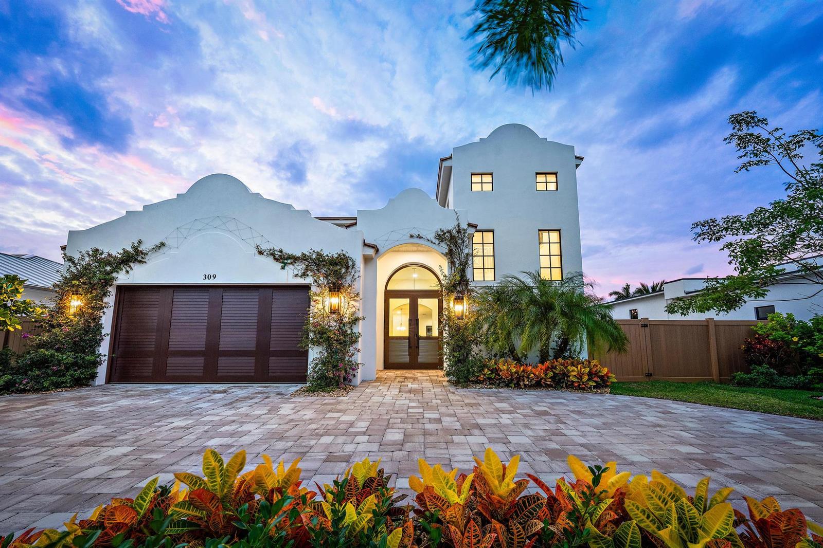 A two-story white stucco house with a brown garage door and arched entryway at dusk — 309 Cascade Lane, Palm Beach Shores FL 33404, PALM BEACH SHORES, FL