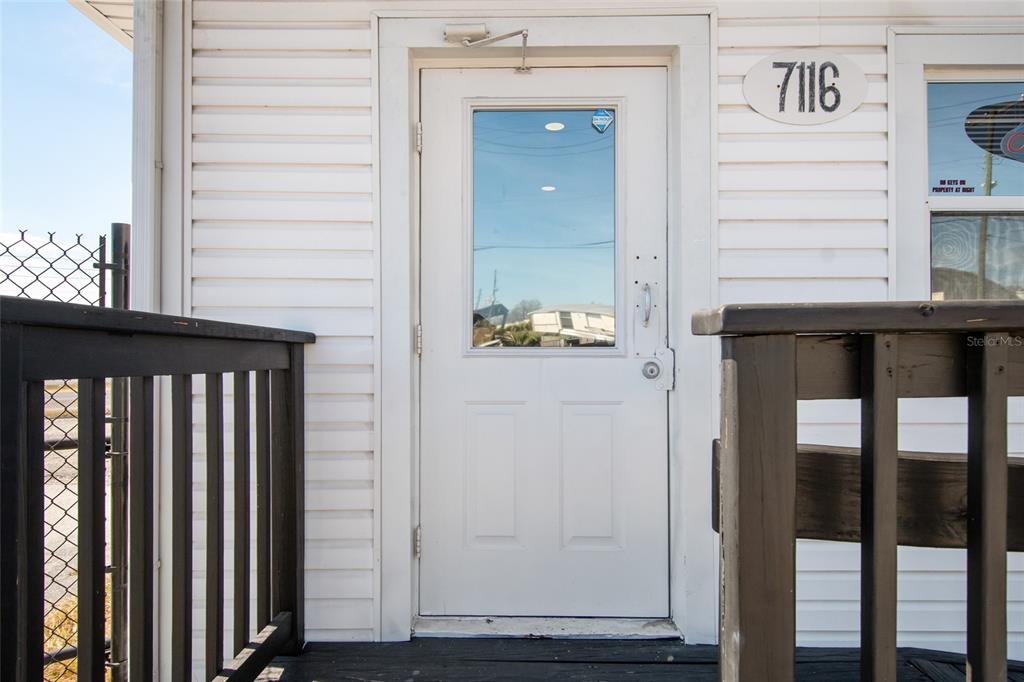 A white door with a glass pane is centered on the exterior siding of a building — 7116 ROSE AVENUE, ORLANDO, FL
