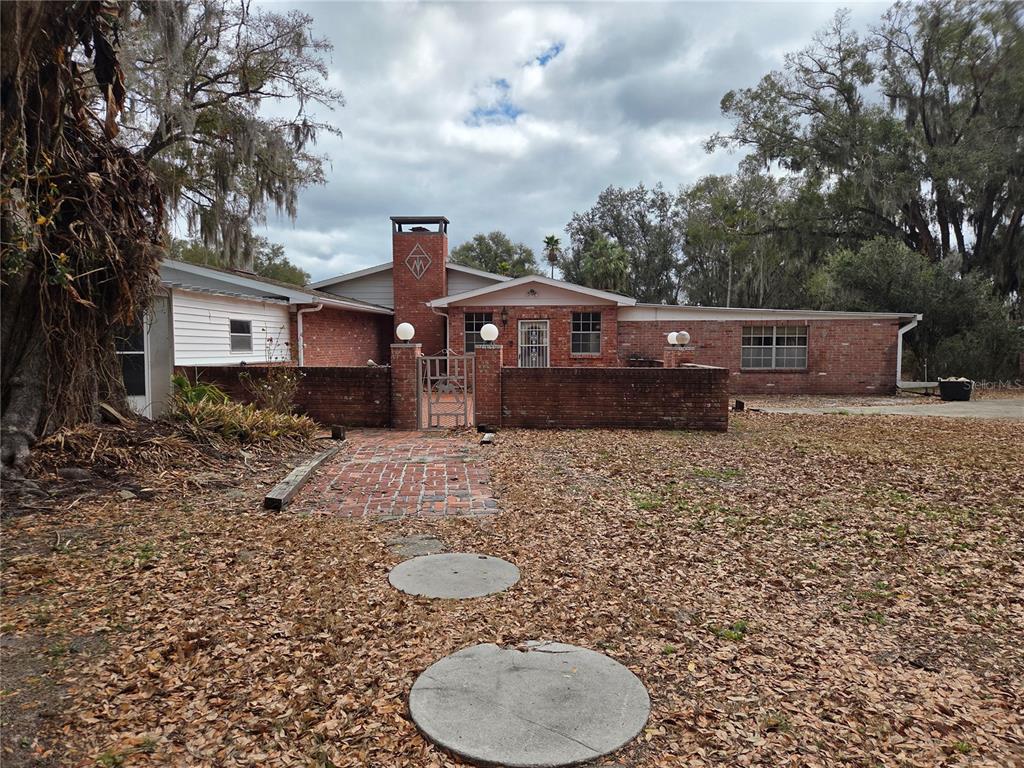 A brick house with a central chimney and a walled courtyard entrance under a cloudy sky — 4911 W SAM ALLEN ROAD, PLANT CITY, FL