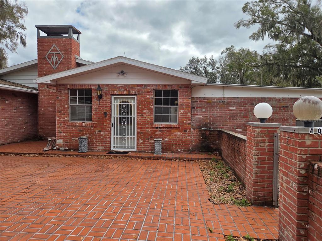 A brick house exterior features a paved courtyard, a chimney with a logo, and windows — 4911 W SAM ALLEN ROAD, PLANT CITY, FL