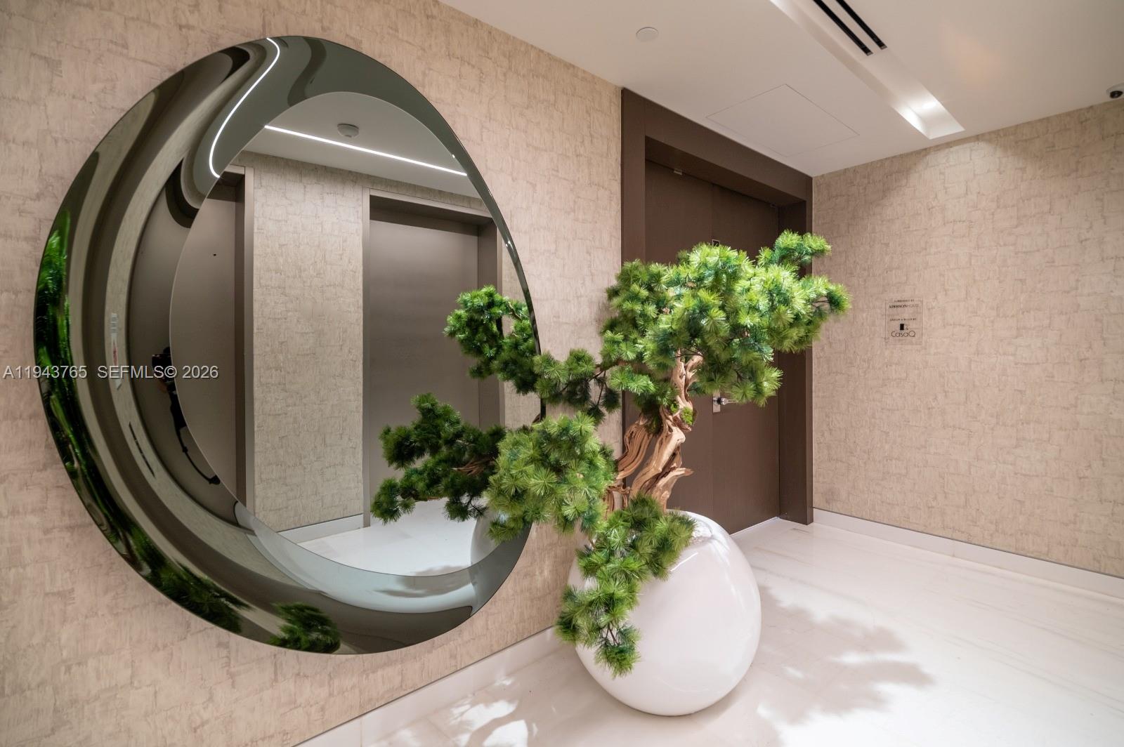 A modern hallway features a large circular mirror, a potted bonsai tree, and textured wallpaper — 300 Biscayne Blvd Way # 3403, Miami FL 33131, MIAMI, FL