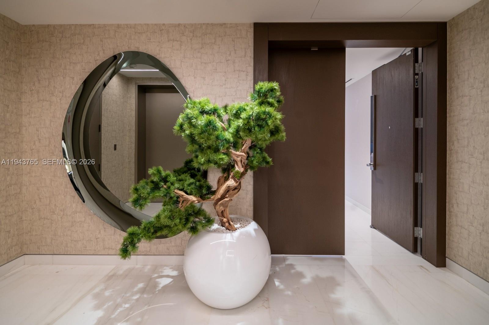 A modern entryway features a large circular mirror, a potted bonsai tree, and dark wood doors — 300 Biscayne Blvd Way # 3403, Miami FL 33131, MIAMI, FL