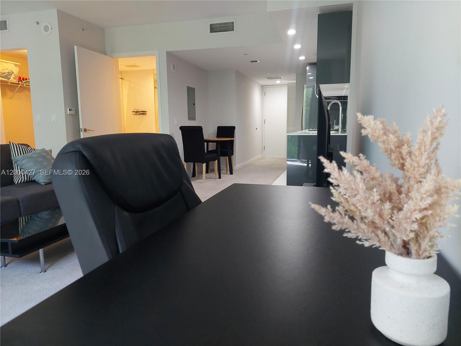 A black desk in the foreground overlooks a living area with a dining set — 31 SE 6th St # 403, Miami FL 33131, MIAMI, FL