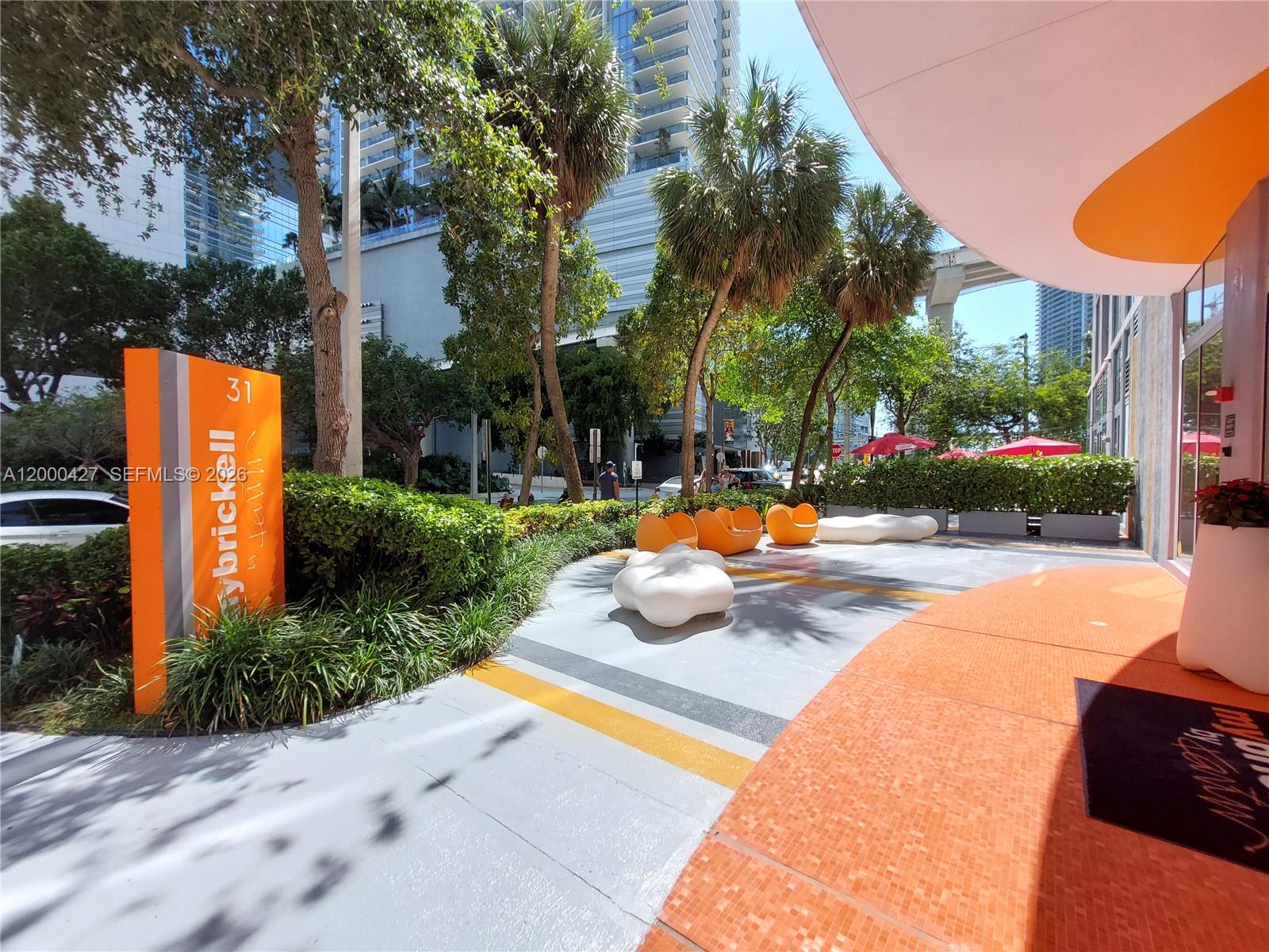 An outdoor patio area features orange signage, modern seating, and palm trees in an urban setting — 31 SE 6th St # 403, Miami FL 33131, MIAMI, FL