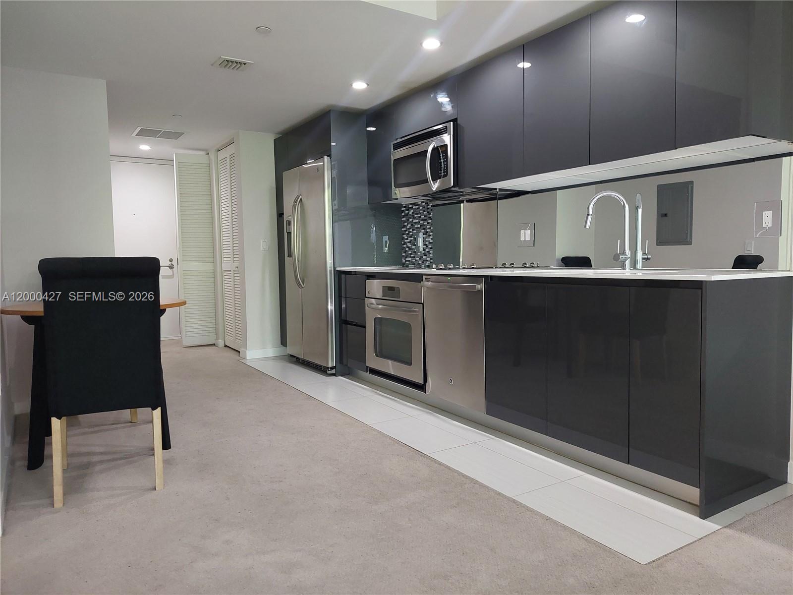 A modern kitchen features dark glossy cabinets, stainless steel appliances, and a mirrored backsplash — 31 SE 6th St # 403, Miami FL 33131, MIAMI, FL