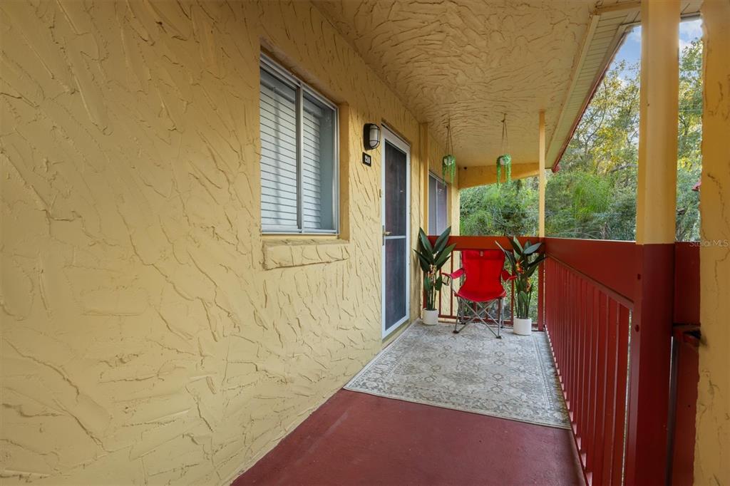 A covered balcony features yellow textured walls, a red floor, and a red metal railing — 400 EL CAMINO DRIVE UNIT 210, WINTER HAVEN, FL