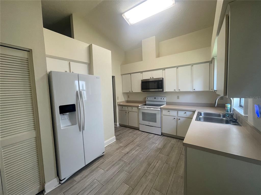 A kitchen features white cabinets, a white refrigerator, a microwave, and light-colored tile flooring — 13104 BARTH PLACE UNIT 13104, RIVERVIEW, FL
